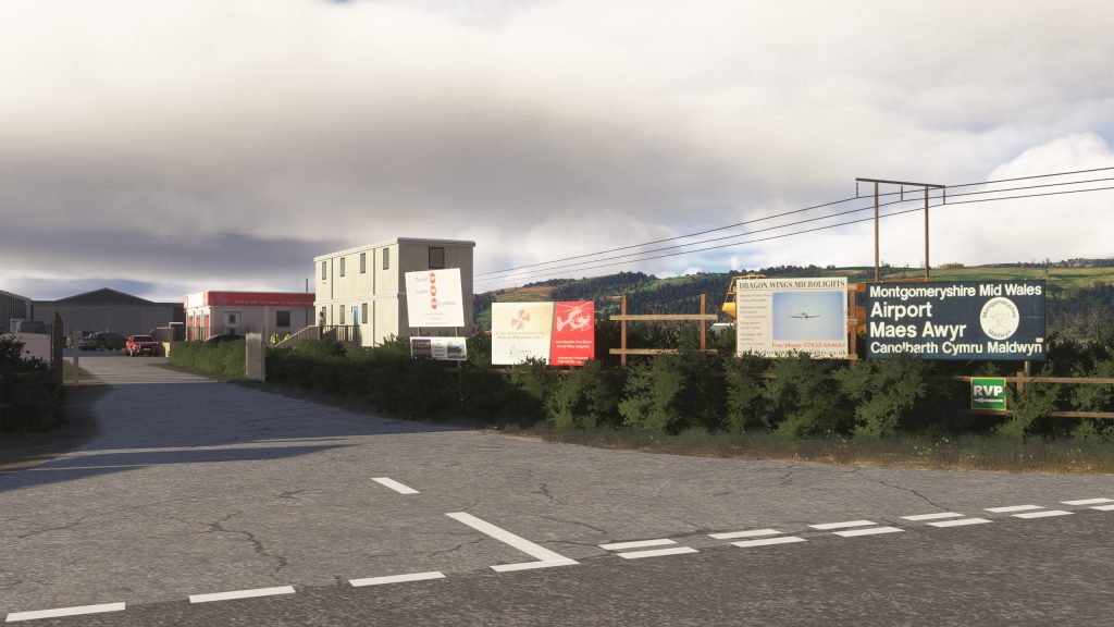 Burning Blue Design's Welshpool airport for MSFS 2020 and MSFS 2024, in sim view of the airport's main entry from local road with signs, building and powerlines. 