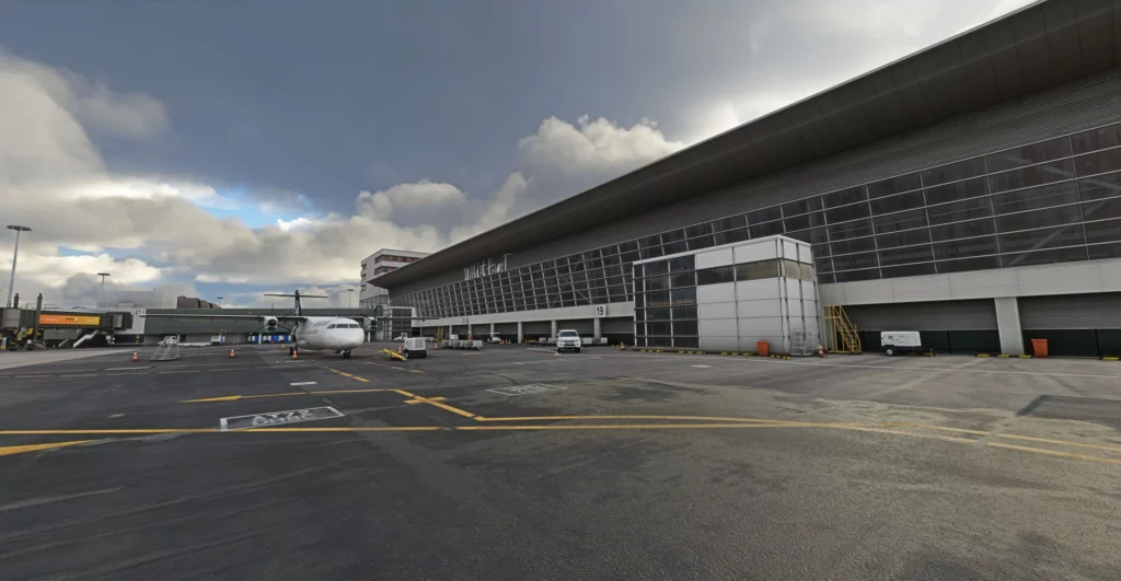 Flightbeam Studios Wellington International Airport scenery in Microsoft Flight Simulator 2020 and 2024, showing the terminal apron and a parked regional aircraft beneath dramatic clouds.