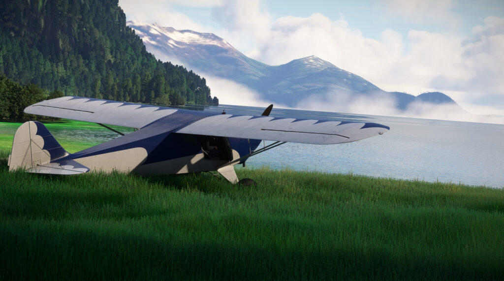 GotFriends Taylorcraft BC-12D parked by a body of water. Mountains in the background.